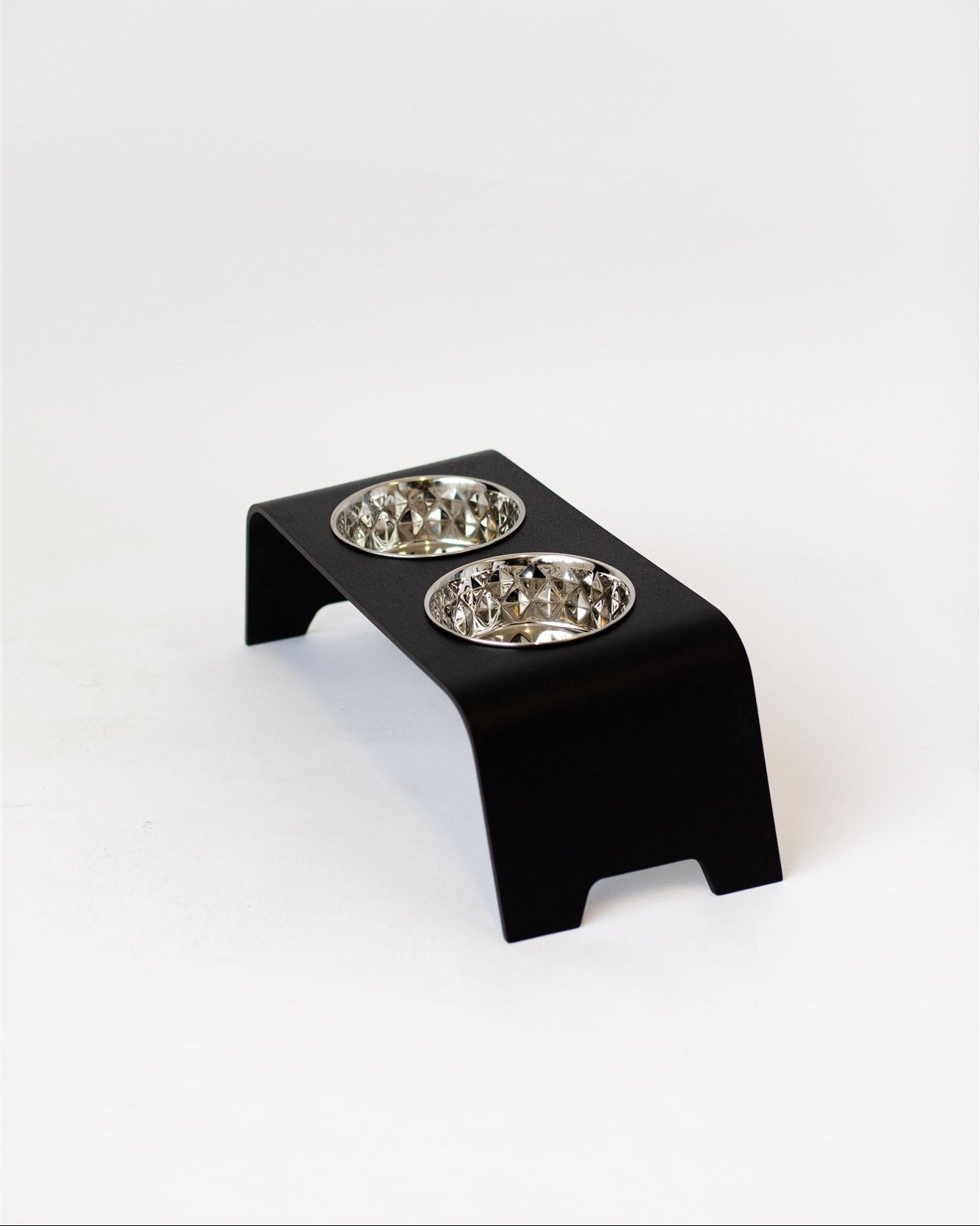 Black elevated pet feeder with two silver bowls on a white background