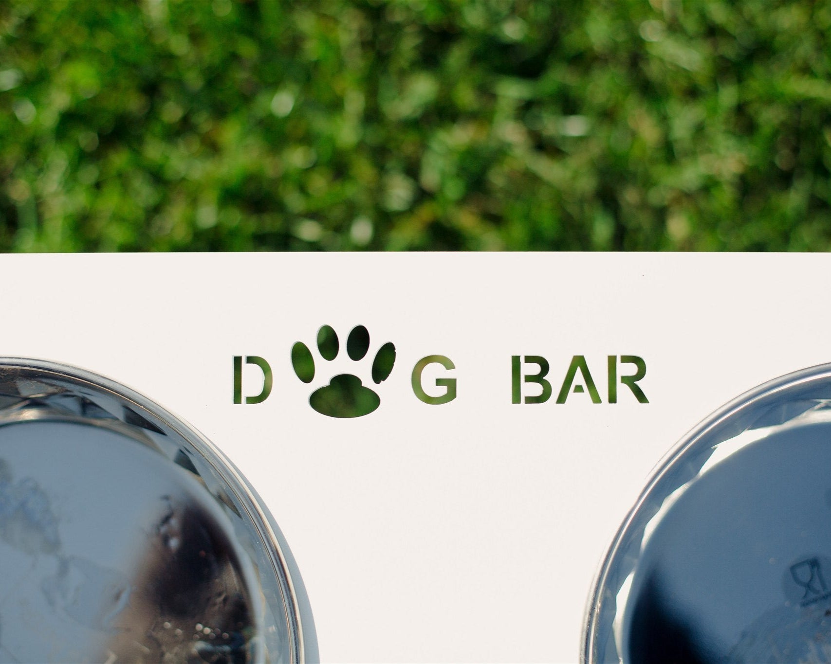 Two metallic dog bowls with 'Dog Bar' logo on a grass background