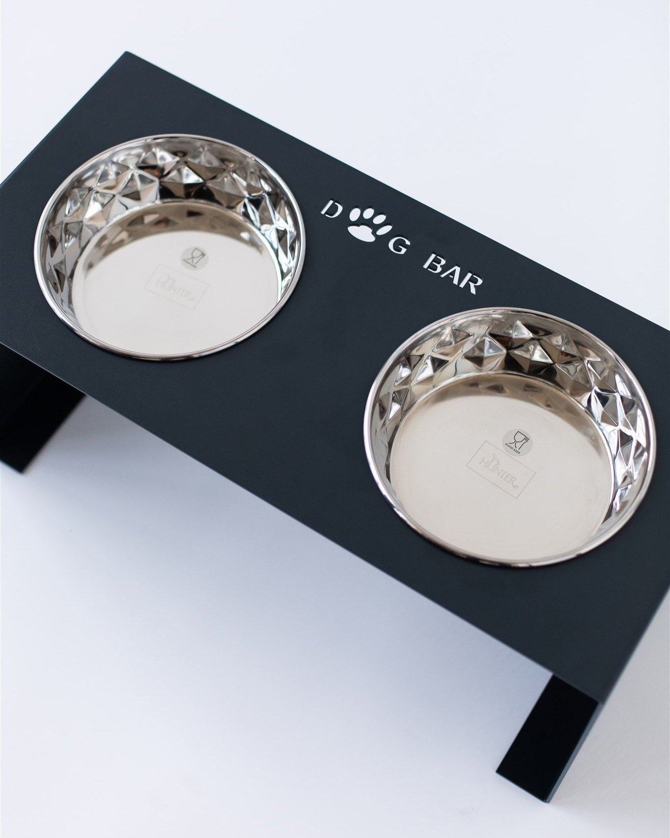 Black elevated dog feeder with two silver bowls on a white background