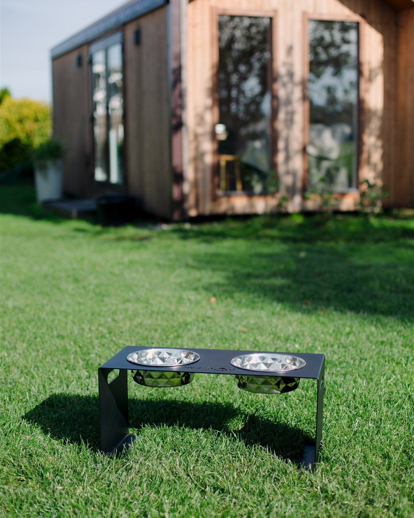 Pet feeder on grass with a wooden cabin in the background