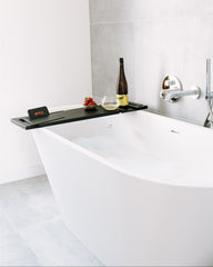 Modern bathroom with a freestanding bathtub, wine bottle, and fruits on a tray.