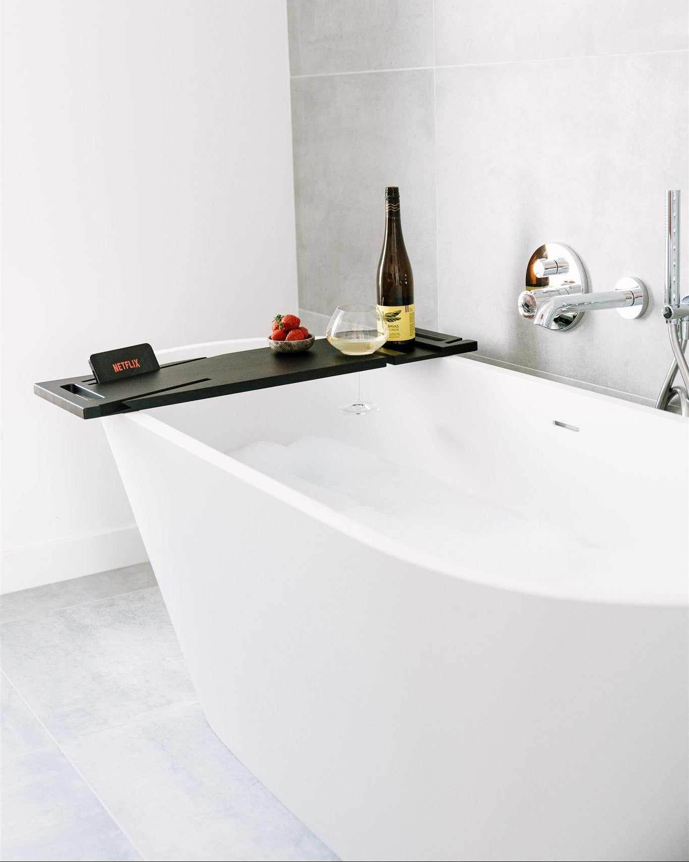 Modern bathroom with a freestanding bathtub, wine bottle, and fruits on a tray.