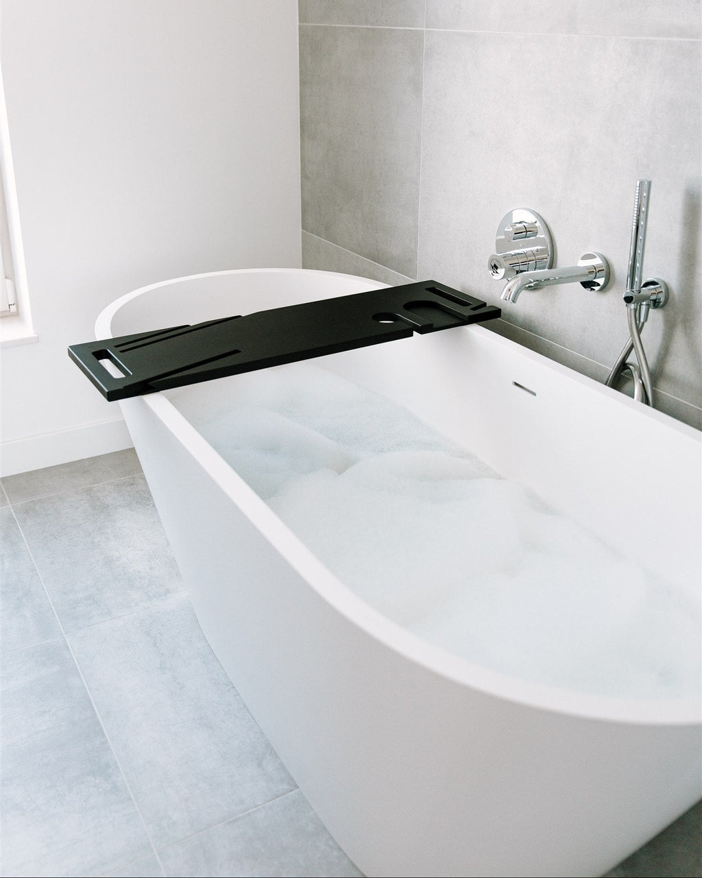 White freestanding bathtub with a black tray in a modern bathroom.