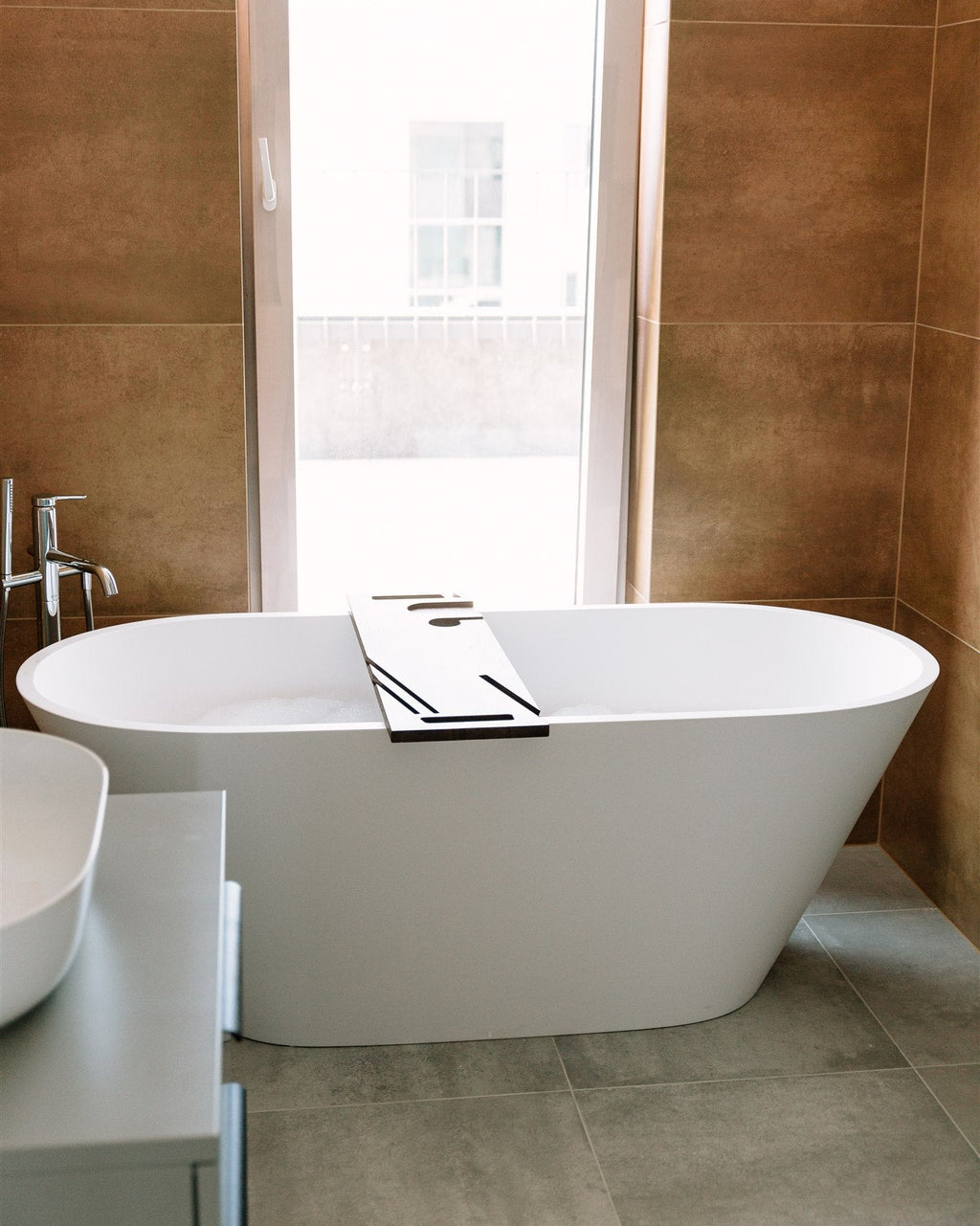 Modern freestanding bathtub in a bathroom with tiled walls and floor.