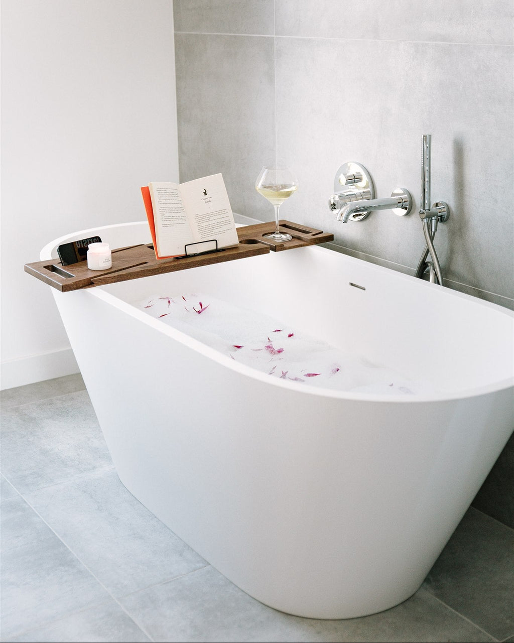 Modern bathroom with a freestanding bathtub, wooden tray, and wine glass.