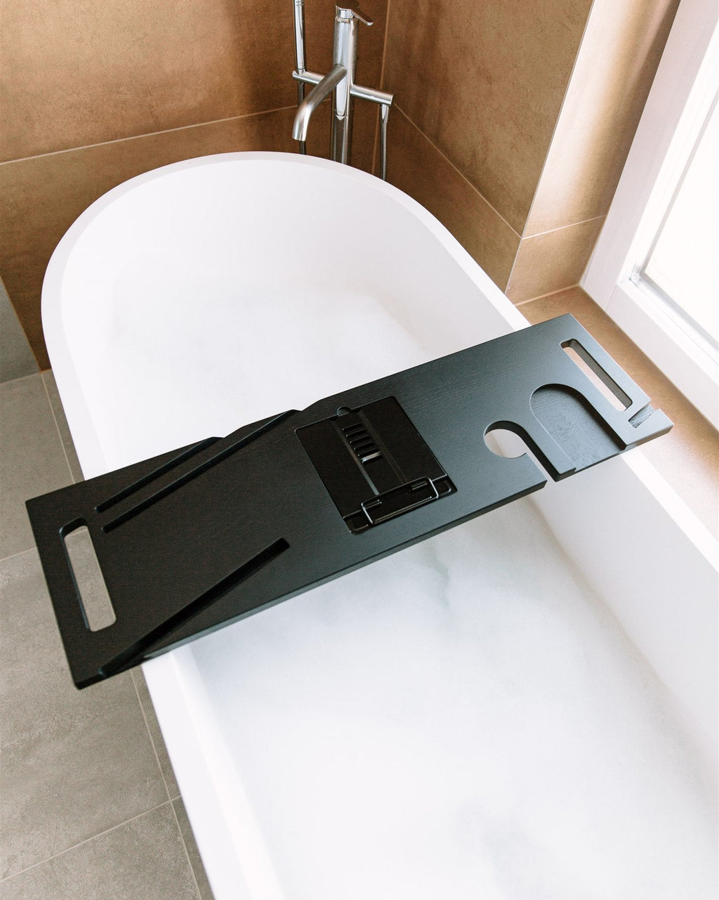 Black bathtub tray on a white bathtub in a bathroom setting
