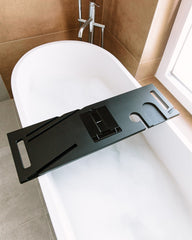 Black bathtub tray on a white bathtub in a bathroom setting