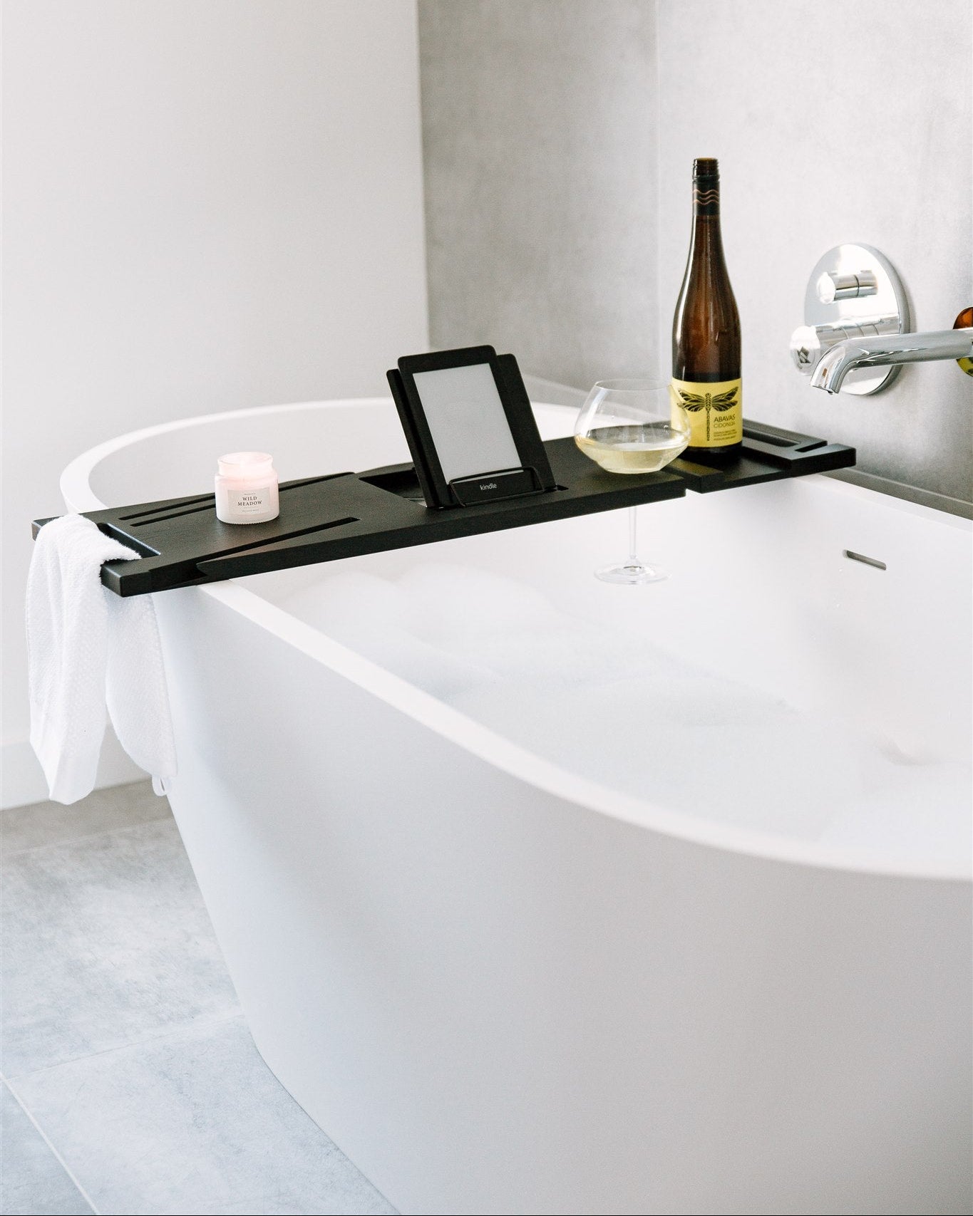 Bath tub with a black tray holding a bottle, candle, and mirror in a bathroom setting.