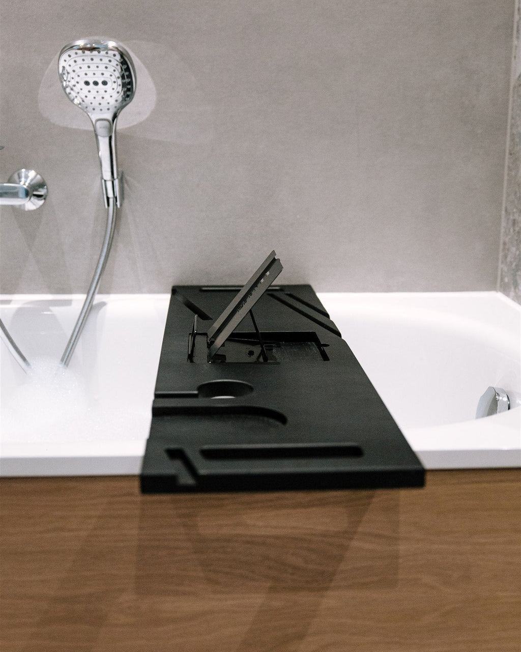 Black rectangular bath mat in front of a bathtub with a shower head and faucet.