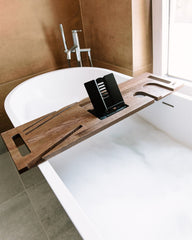 Wooden bathtub tray with a tablet stand on a white bathtub in a bathroom.