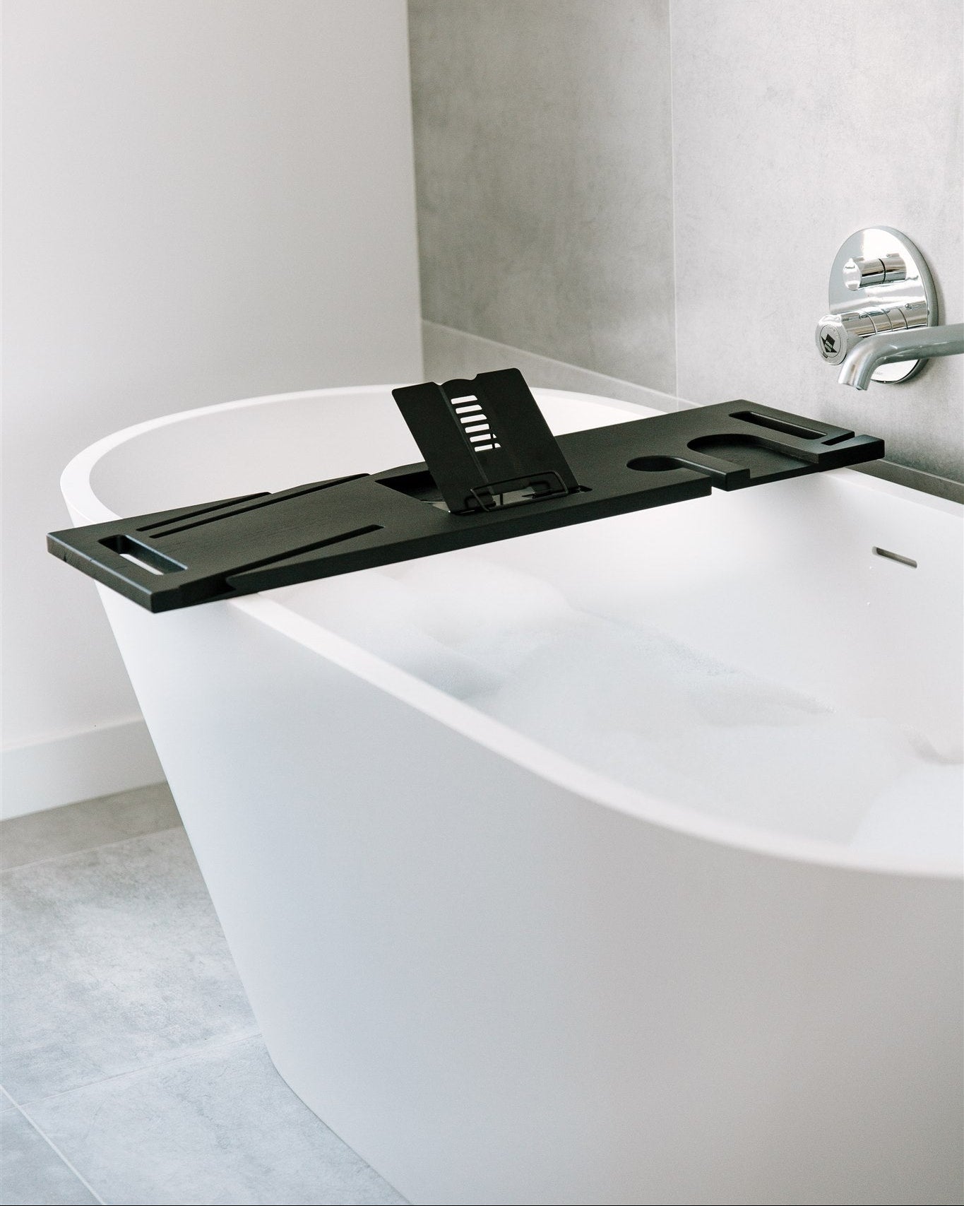 White freestanding bathtub with a black bathtub tray in a modern bathroom.