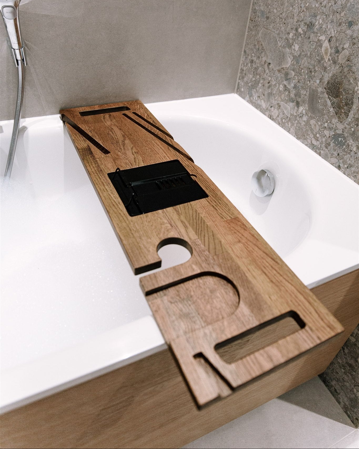 Wooden bathtub tray with cutouts on a white bathtub in a bathroom setting.