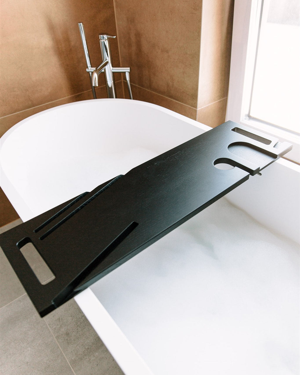 Black bathtub tray in a bathroom setting with a white bathtub and tiled walls.