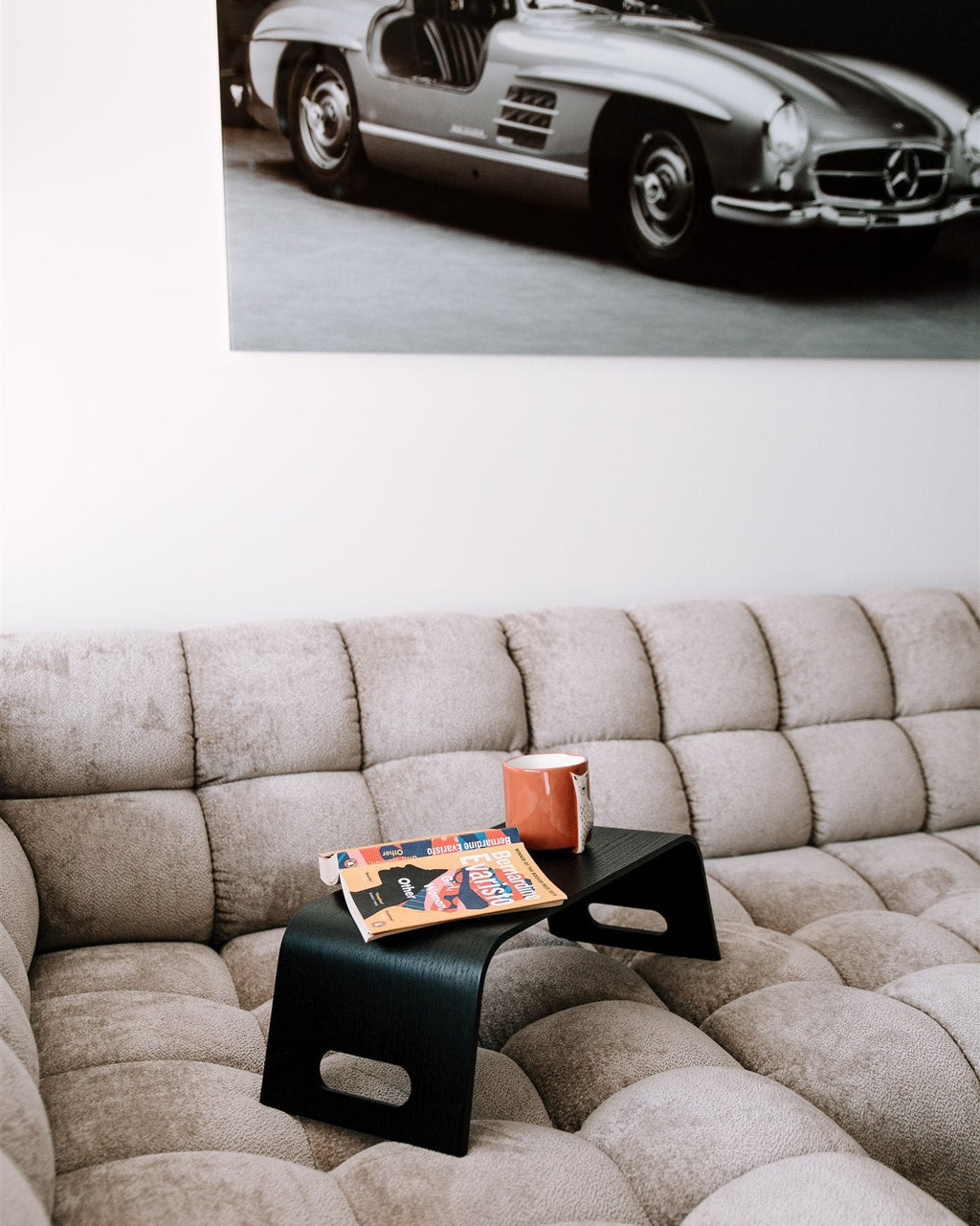 Beige sofa with a small table and books, above which is a black and white photo of a classic car.
