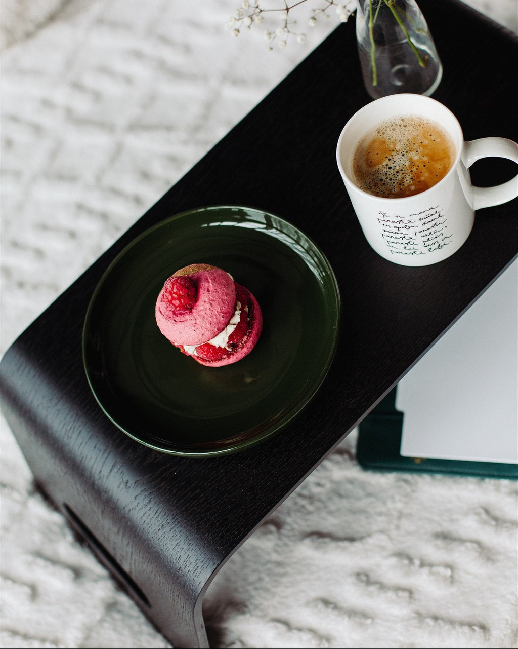 Cup of coffee and dessert on a black tray with a vase of flowers, on a textured surface.