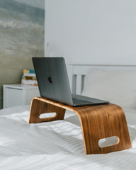 Wooden laptop stand with a laptop on a bed