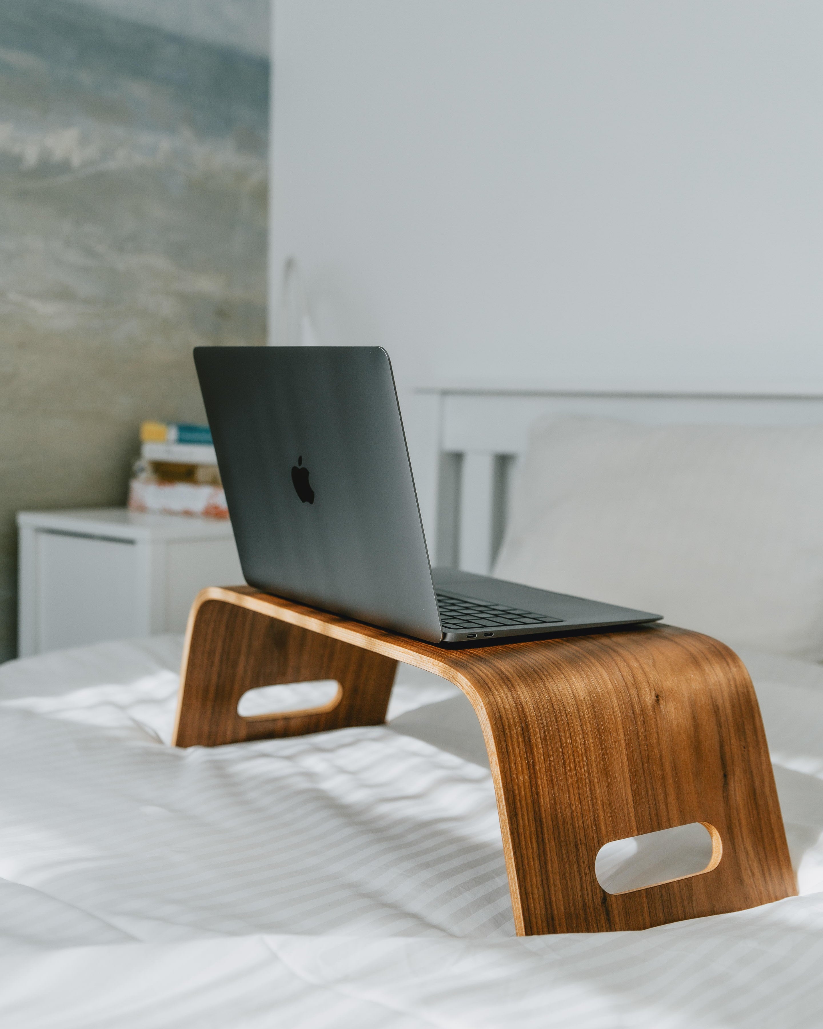 Wooden laptop stand with a laptop on a bed