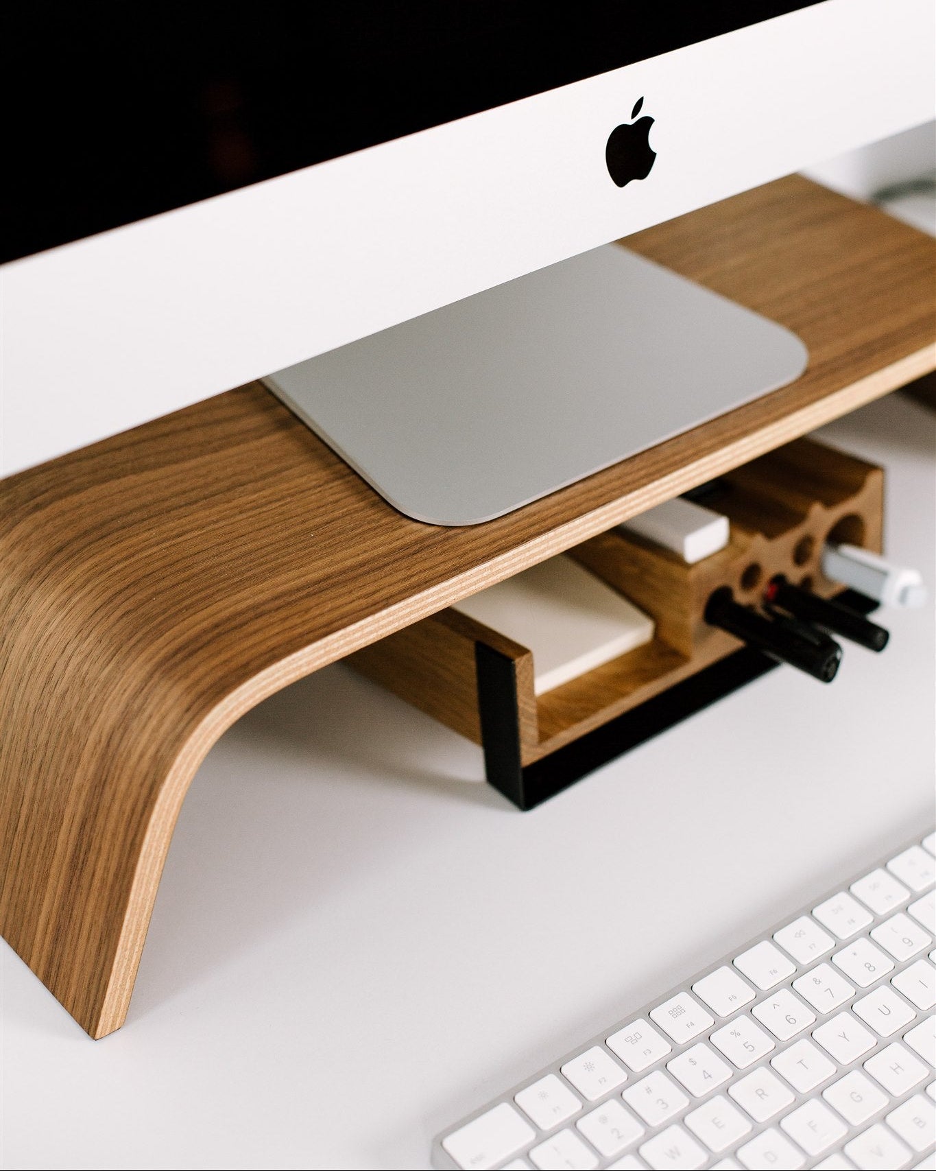 Wooden monitor stand with a computer setup on a white surface
