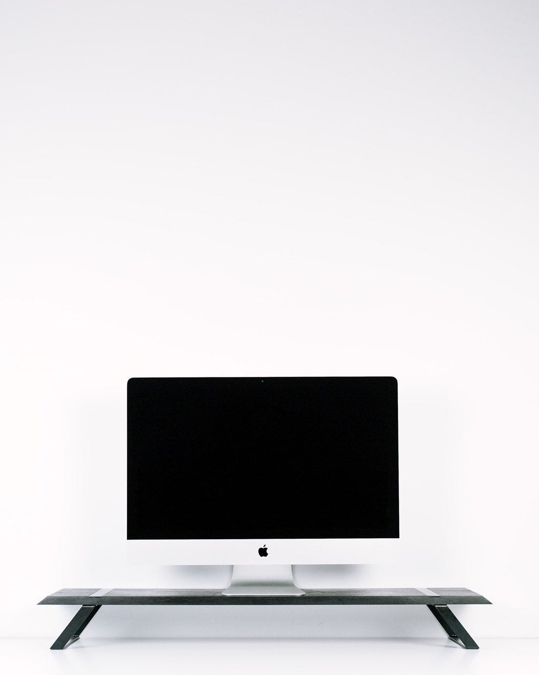 Black computer monitor on a white desk with a white wall background