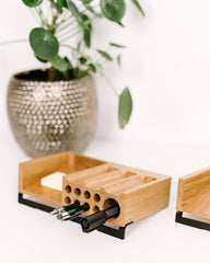 Wooden pen holder with multiple pen holders on a white surface with a plant in the background.