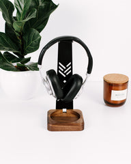 Black headphones on a wooden stand with a candle and plant in the background