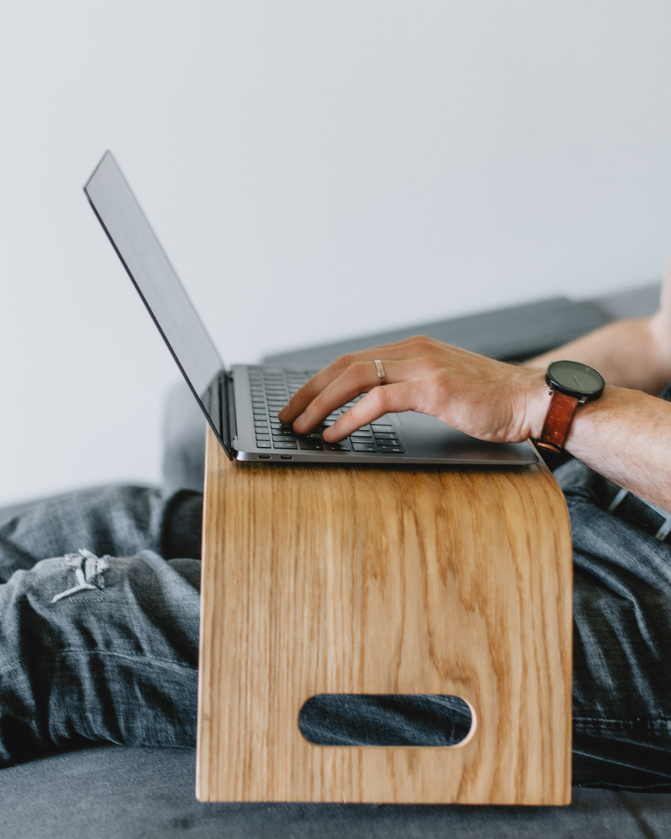 Person using a laptop on a wooden stand with a plain background