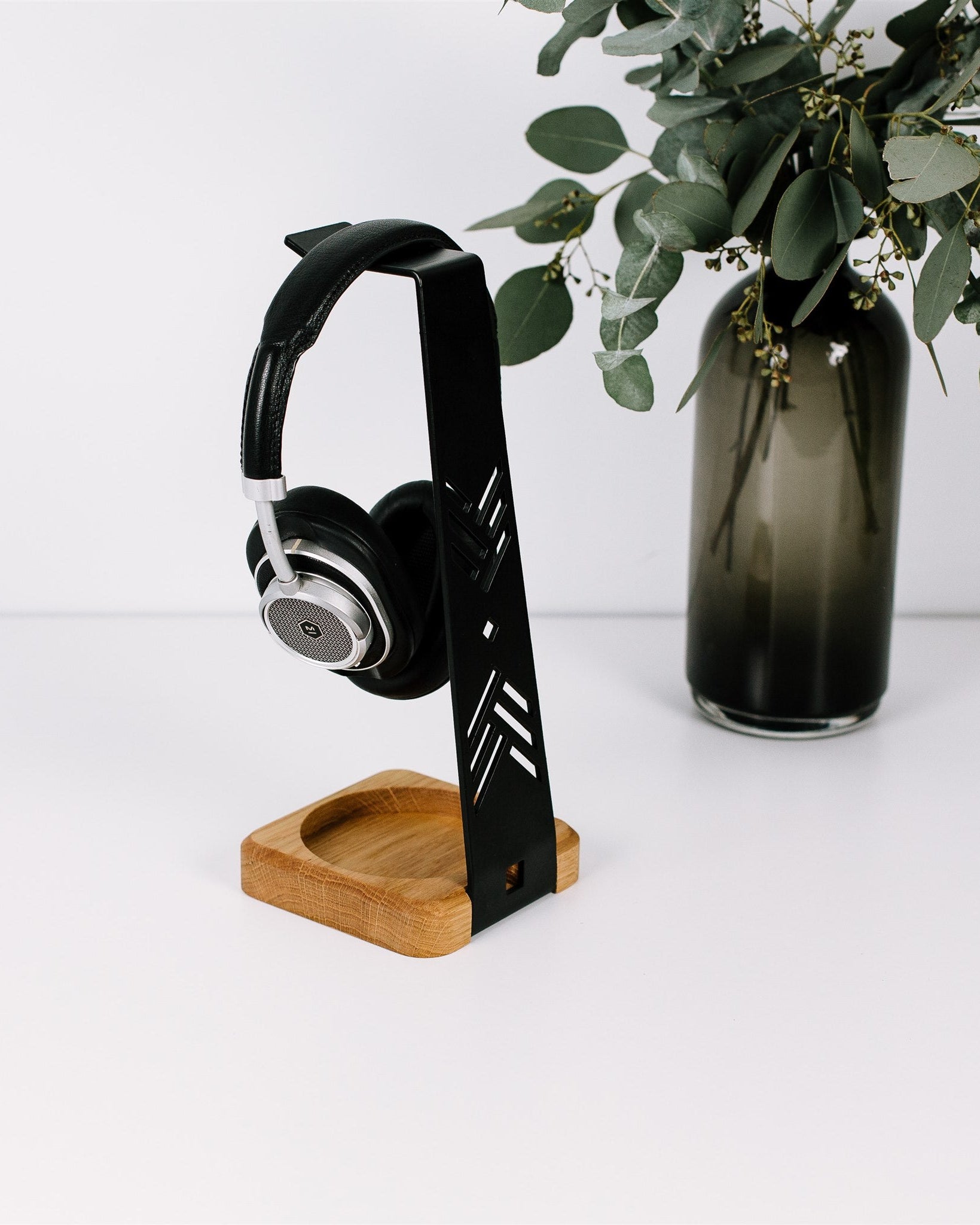 Black headphones on a wooden stand with a vase of greenery in the background