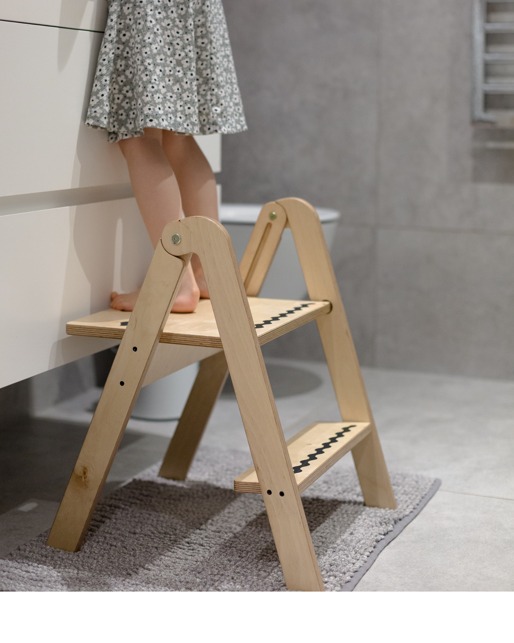 Wooden step stool with a person wearing a floral dress standing on it in a bathroom setting.