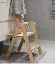 Wooden step stool with a person wearing a floral dress standing on it in a bathroom setting.