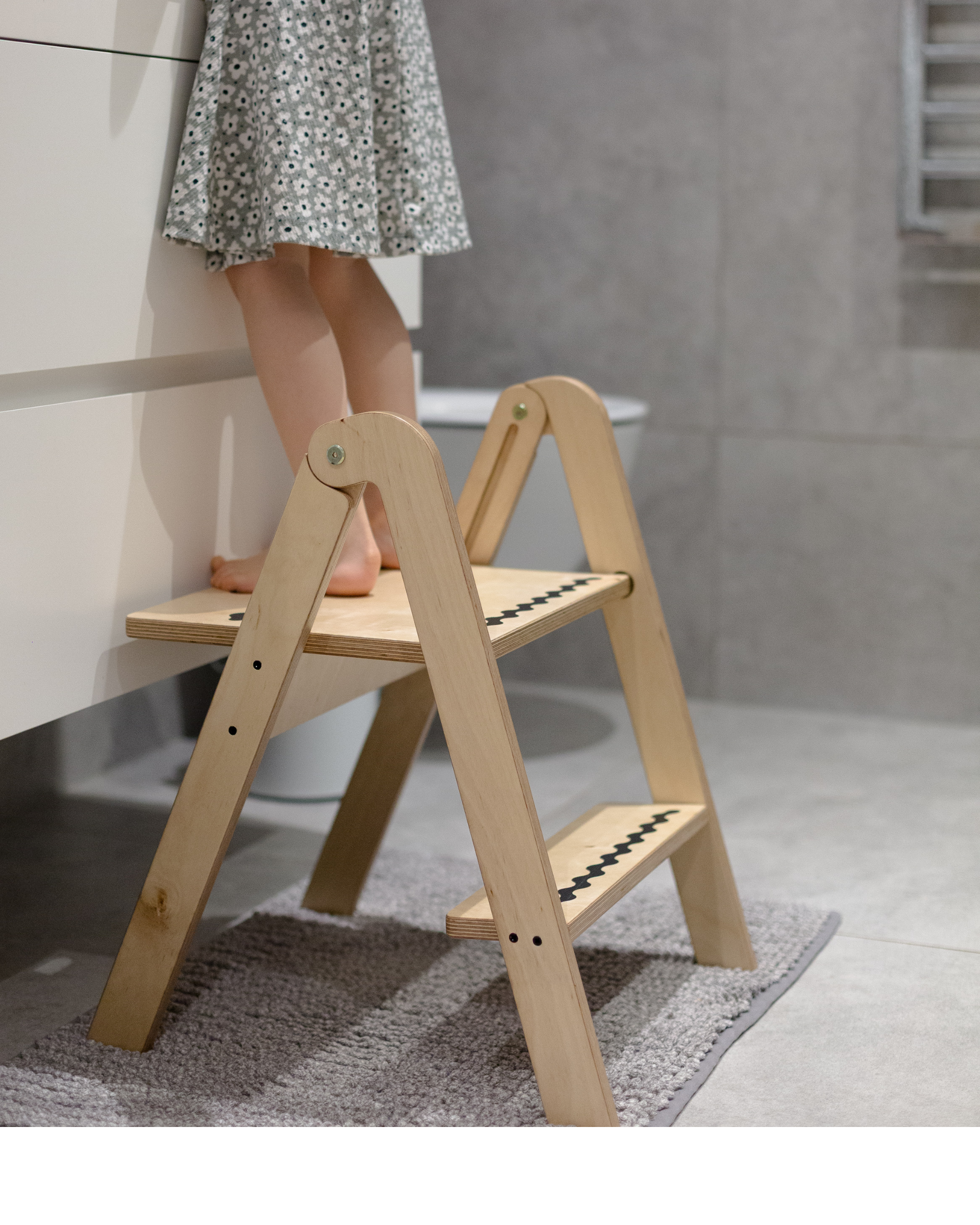 Wooden step stool with a person wearing a floral dress standing on it in a bathroom setting.