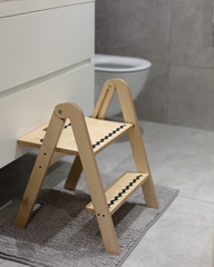Wooden step stool on a bathroom floor with a toilet in the background