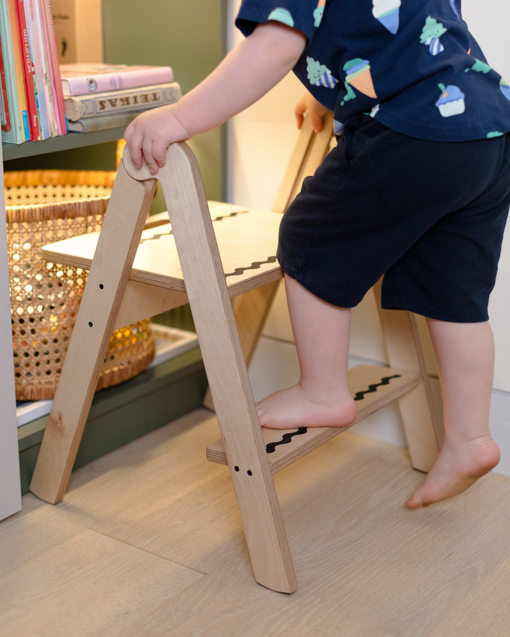 Child climbing a wooden step stool in a home setting