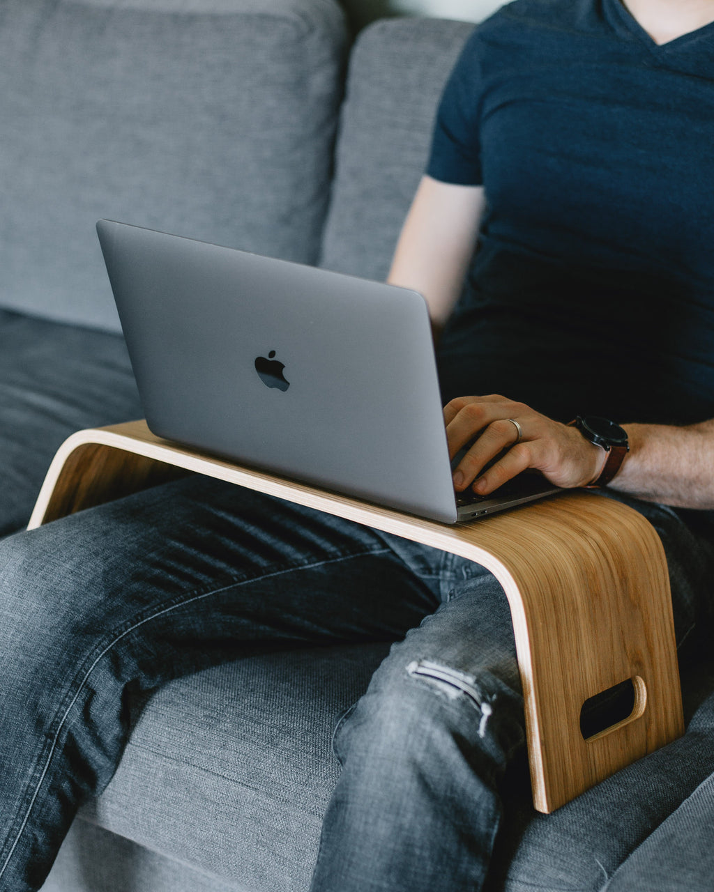 Person using a laptop on a wooden lap desk while sitting on a couch.