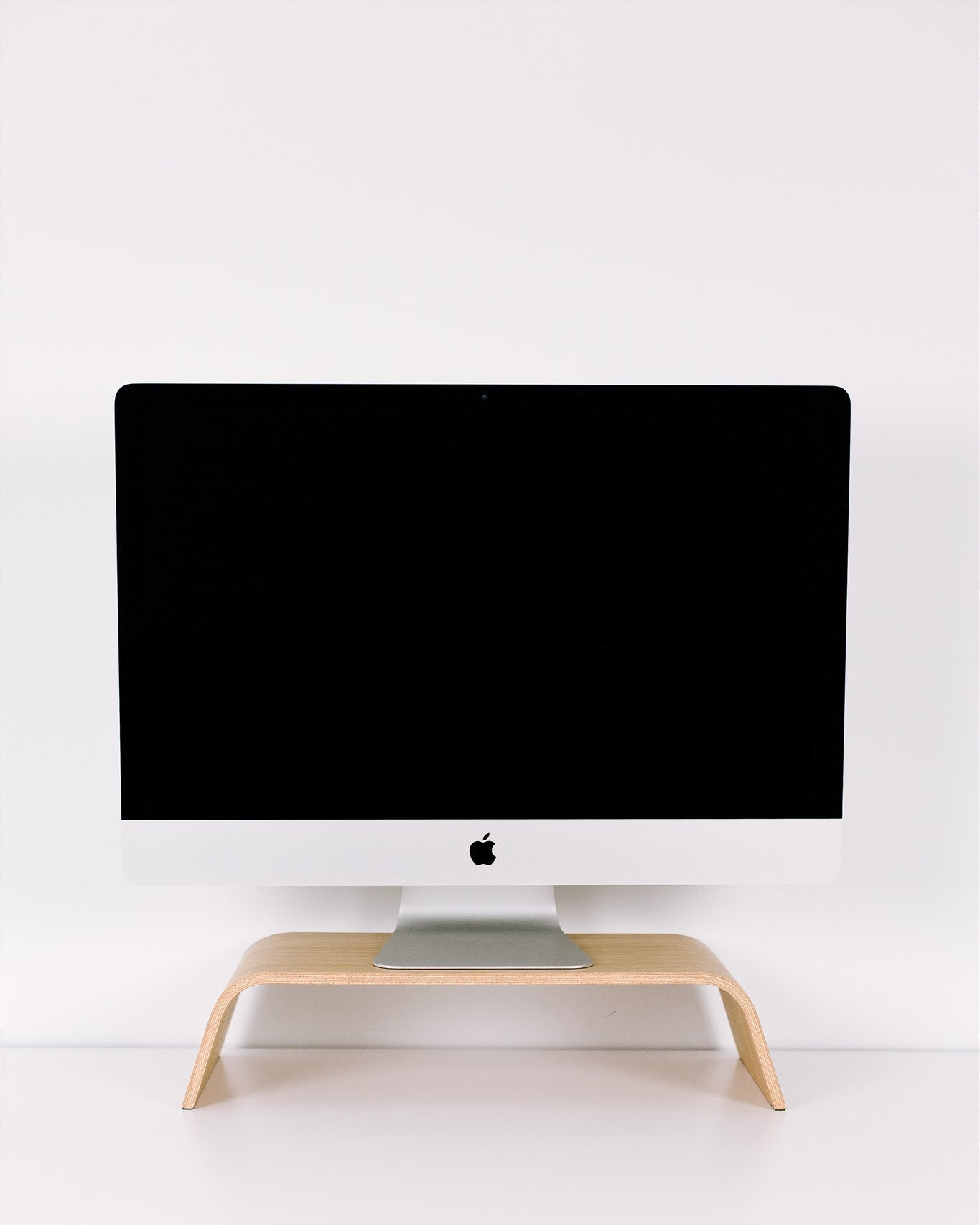 Black computer monitor on a wooden stand against a white wall