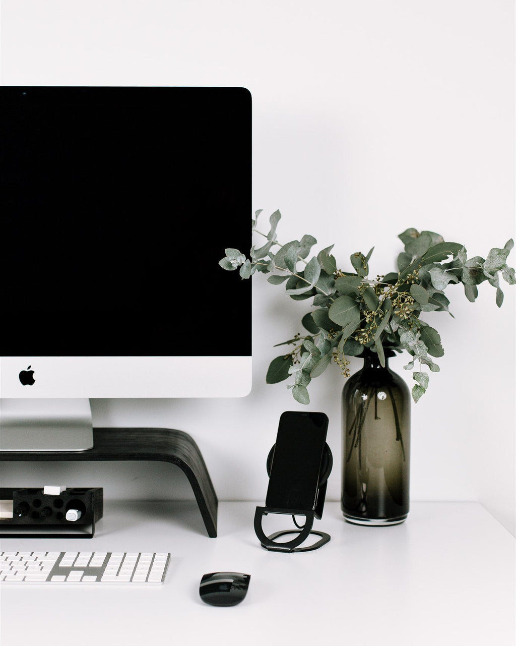Modern office desk with computer monitor, keyboard, mouse, and decorative vase with greenery.
