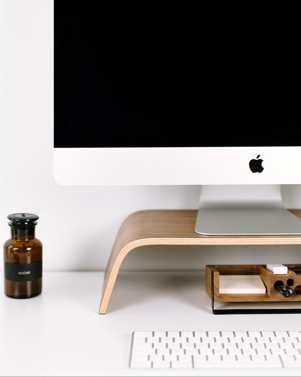 Computer monitor on a wooden stand with a bottle and keyboard in a minimalistic setup