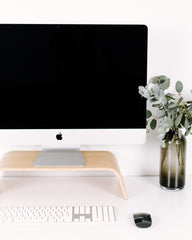 Modern office desk setup with computer monitor, keyboard, mouse, and decorative vase with flowers.