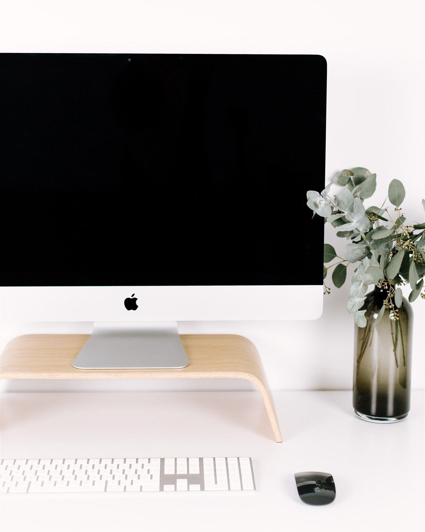 Modern office desk setup with computer monitor, keyboard, mouse, and decorative vase with flowers.