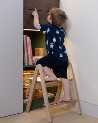 Child using a wooden step stool to reach a bookshelf.