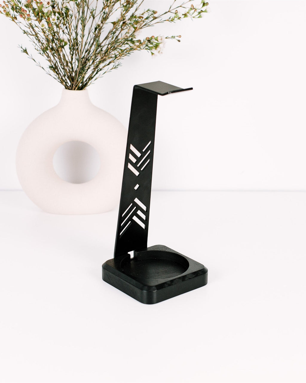 Black phone stand with decorative vase and plant on a white background
