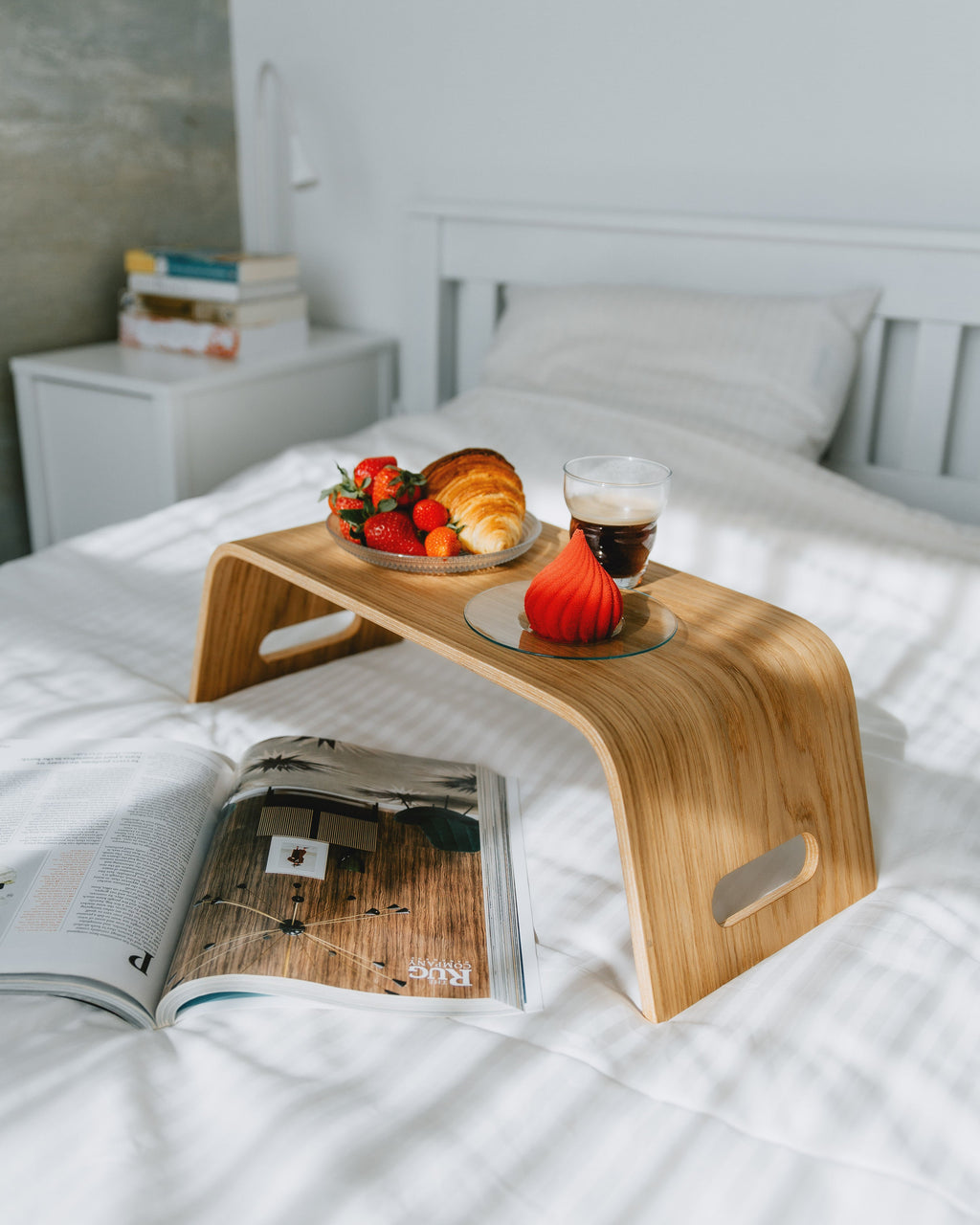 Wooden lap desk on a bed with a magazine, fruit, and coffee.