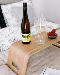 Wine bottle and glass on a wooden tray with strawberries on a sofa