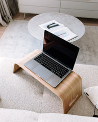 Laptop on a wooden stand on a sofa with a coffee table in the background