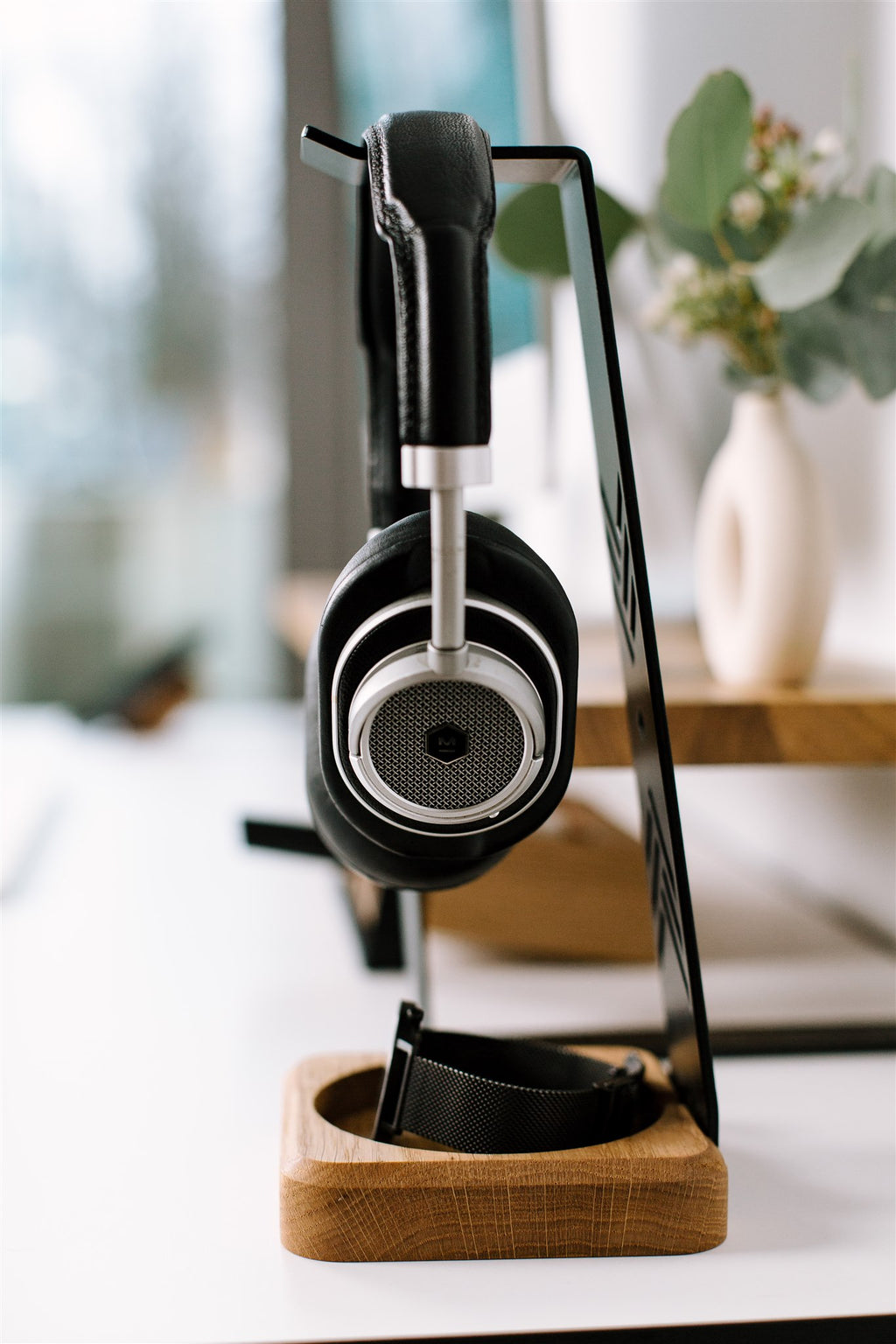 Pair of black headphones on a wooden stand with a blurred indoor background