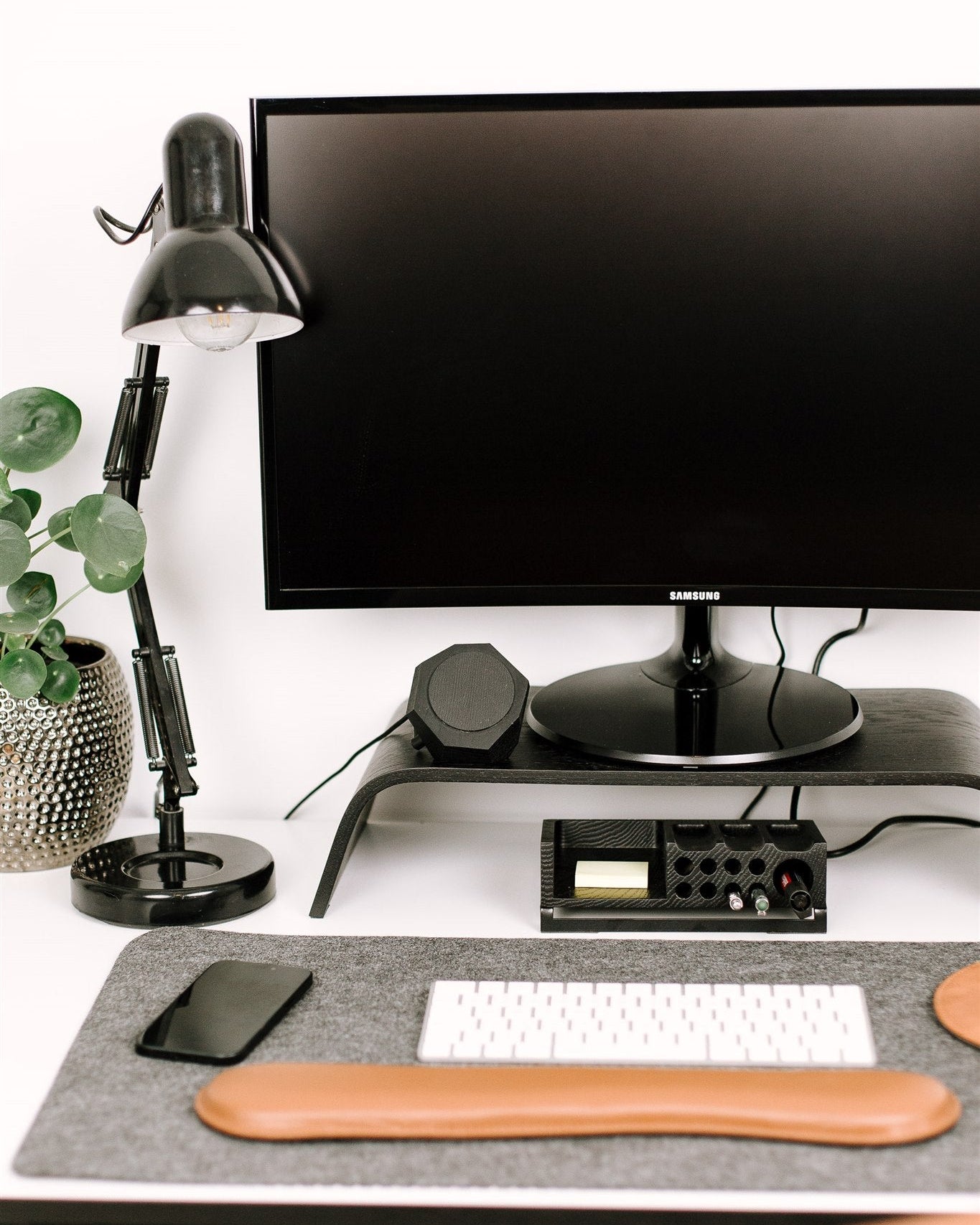 Modern office desk setup with computer monitor, lamp, and keyboard on a white surface.