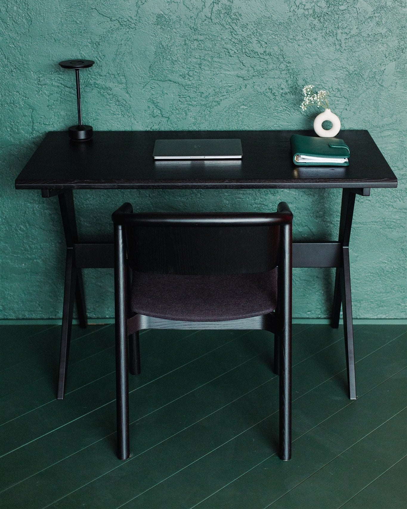 Black desk with chair against a teal wall