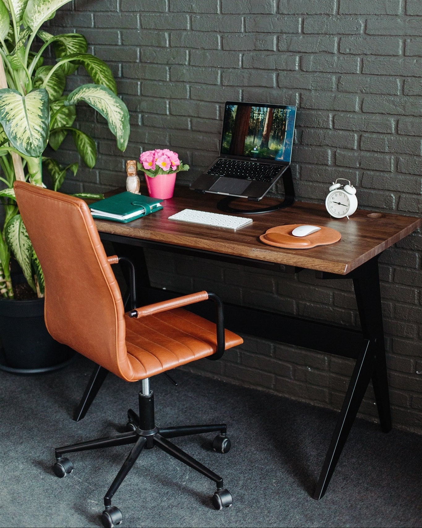 Home office setup with a wooden desk, leather chair, and decorative items against a brick wall.