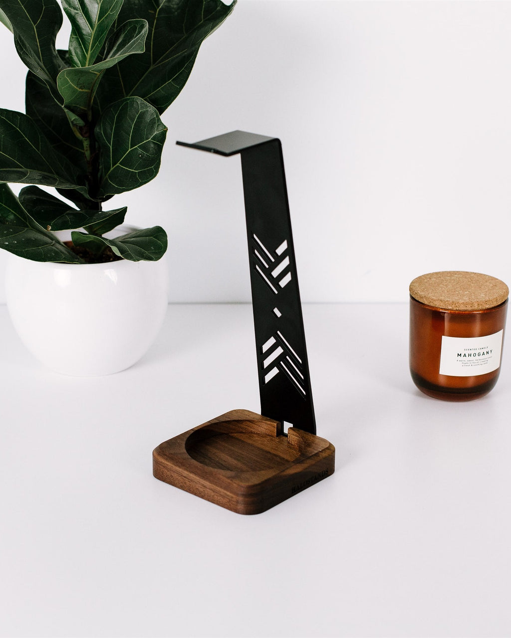 Black metal desk lamp with wooden base next to a candle on a white surface with a plant in the background