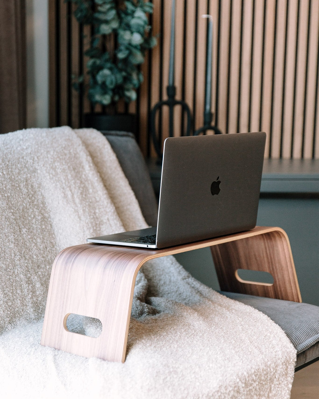 Laptop on a wooden lap desk with a cozy blanket and plant in the background