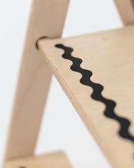 Close-up of a wooden step stool with a black wavy line design on a white background